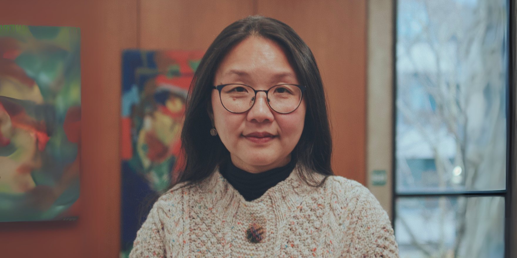 Dr Lai Ma photographed in front of a wall of paintings and a large glass window