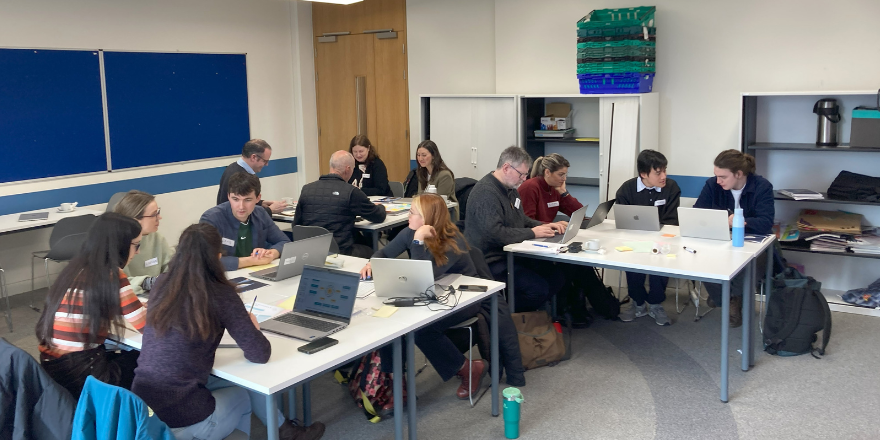 A group of individuals sitting at desks participating in a group activity during TROPIC winter school.