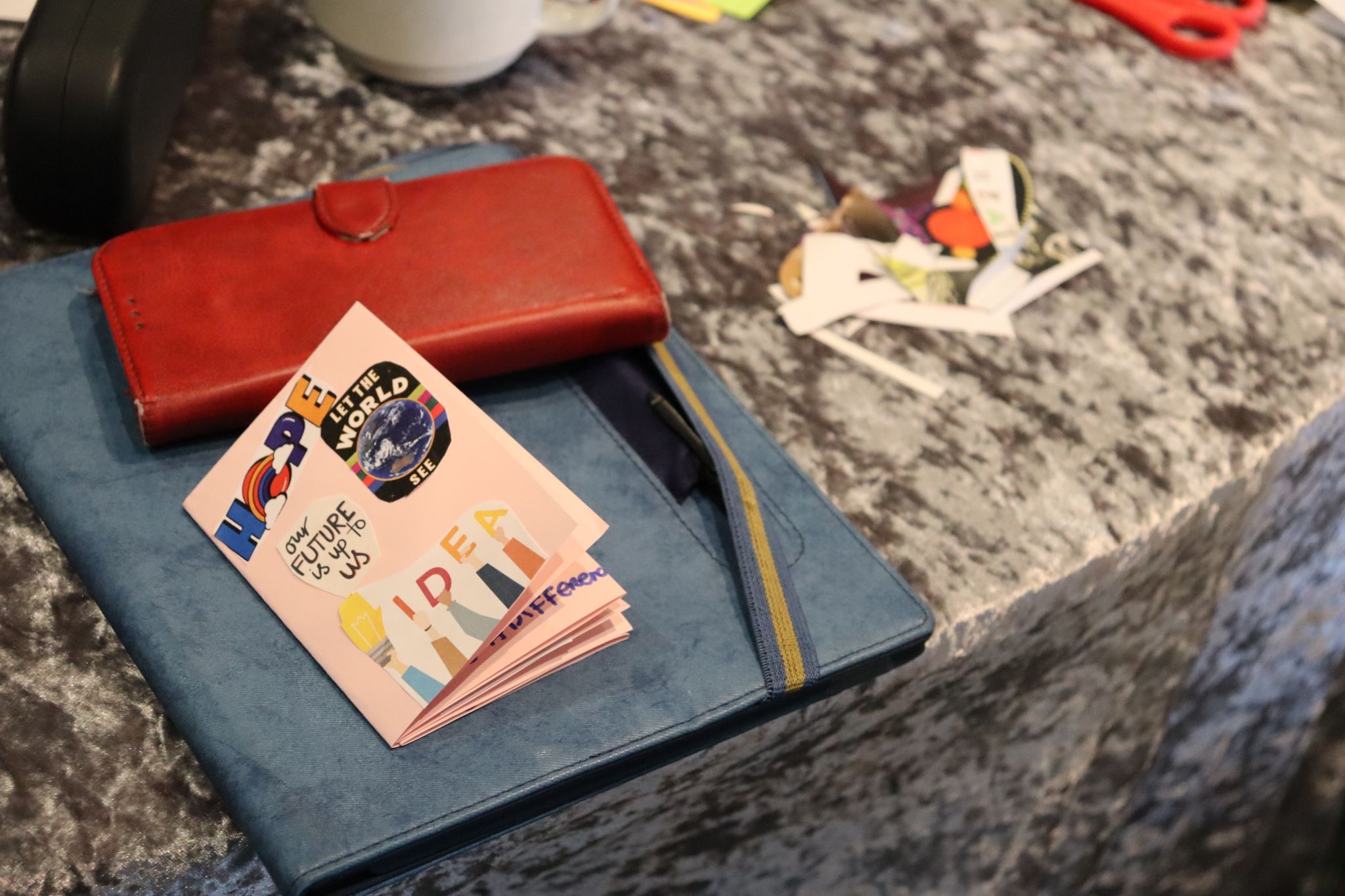 ENGAGED workshop A vivid red leather wallet takes center stage on a monochrome tablecloth. A colorful handmade cartoon poster with open science references on it and a blue book add visual interest, creating a playful yet studious ambiance.