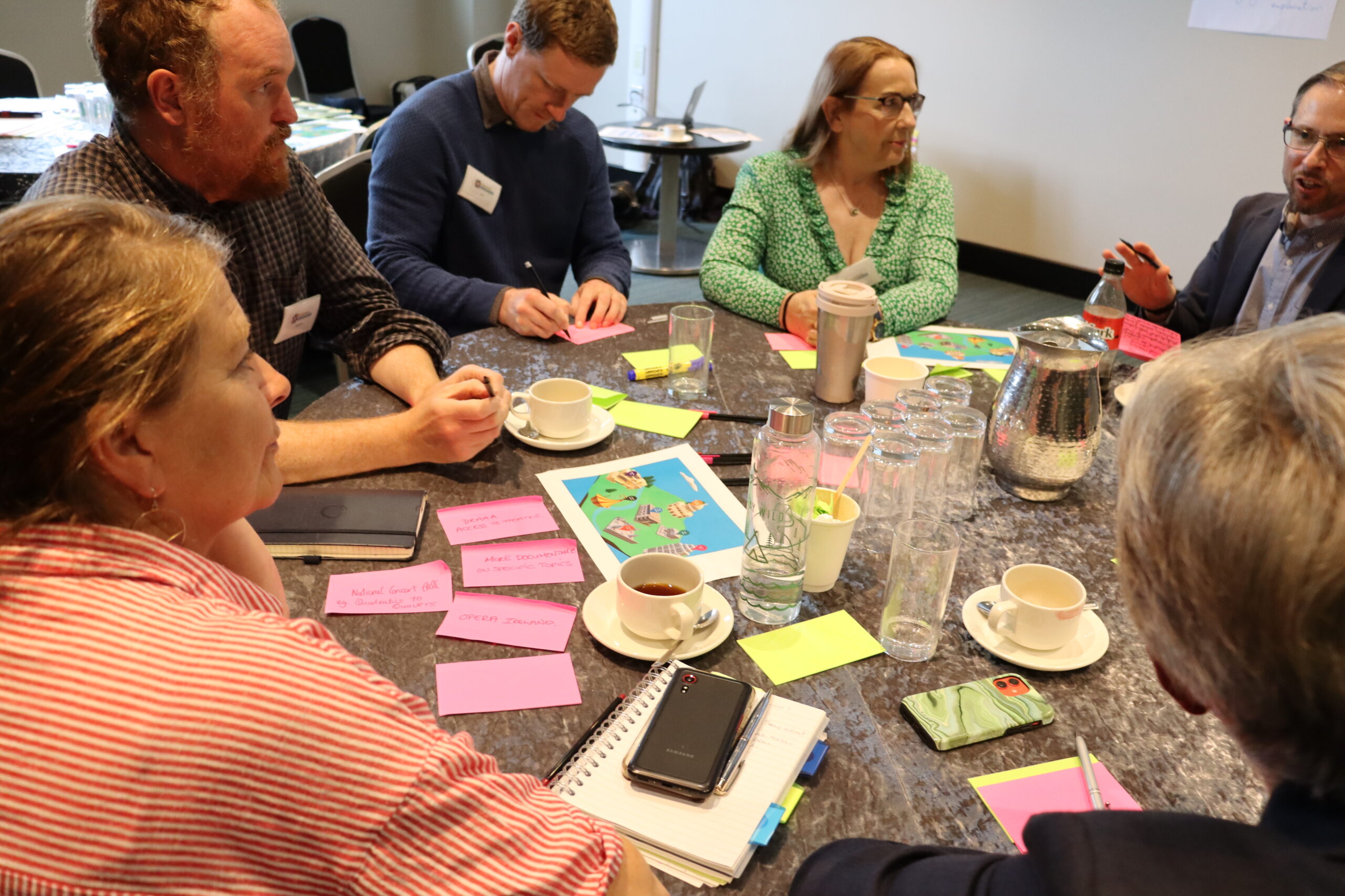 Participants collaborate around a table with sticky notes and notebooks during an ENGAGED collective intelligence workshop.